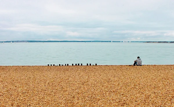 Único homem sentado na praia de seixos — Fotografia de Stock
