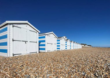 Hastings, Doğu Sussex, İngiltere - 03.15.2022: Yaz günü Hastings sahil kulübeleri çakıl taşı plajındaki güzel mavi çizgili kulübeler