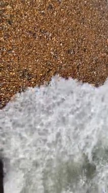 Çakıl taşları, arkaplandan çekilen dalgalarla dolu bir kumsalda yüzüyor. 