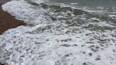 Çakıl taşları, arkaplandan çekilen dalgalarla dolu bir kumsalda yüzüyor. 