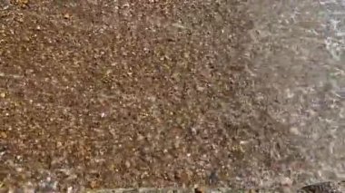 Çakıl taşları, arkaplandan çekilen dalgalarla dolu bir kumsalda yüzüyor. 