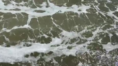 Çakıl taşları, arkaplandan çekilen dalgalarla dolu bir kumsalda yüzüyor. 