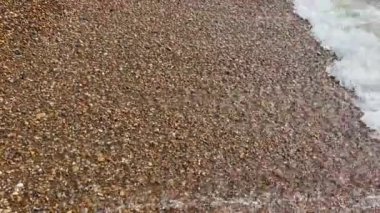 Çakıl taşları, arkaplandan çekilen dalgalarla dolu bir kumsalda yüzüyor. 
