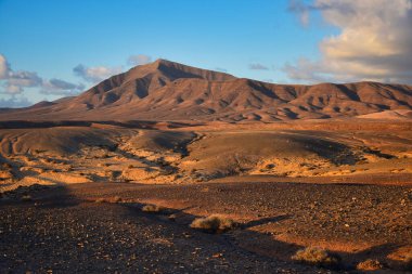 Costa de Papagayo, Lanzarote, İspanya 'da. Gün batımında Los Ajaches sıradağları. Mavi gökyüzünde bulutlarla güneşli bir akşam, altın saat..