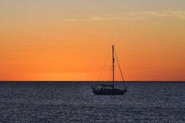 Gün batımında okyanusta turuncu gökyüzü olan küçük bir yelkenli. Lanzarote, İspanya.