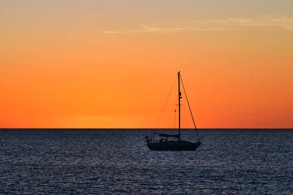 Gün batımında okyanusta turuncu gökyüzü olan küçük bir yelkenli. Lanzarote, İspanya.
