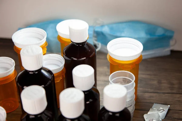 Cough medicine, medication cups, open and empty medication blister packs, and prescription medication bottles with medical masks in the background