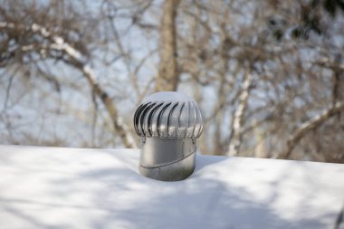 Shiny, snow-dusted whirlybird air vent on a snow-covered roof clipart