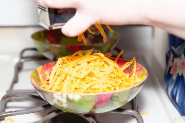 Parlak bir kâseye peynir parçalamak için rende kullanan bir kadının elleri.