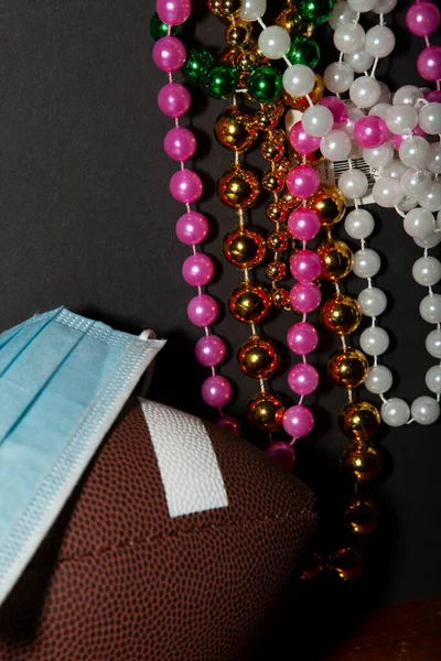 Blue paper mask on a football with pink, gold, green, and white beads in the background