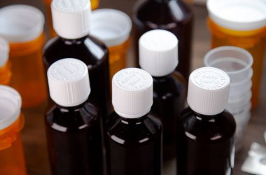 Öksürük şurubu şişeleri, ilaç bardakları, açık ilaç paketleri ve masada ilaç şişeleri.