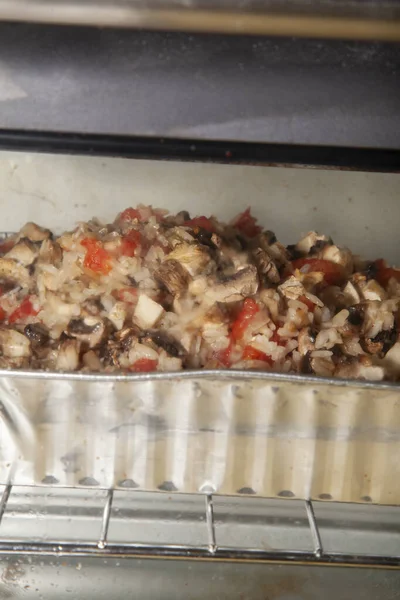 Sliced mushrooms, diced tomato, and diced chilis in rice cooking in an oven