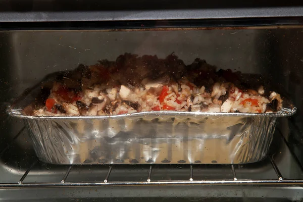 Sliced mushrooms, diced tomato, and diced chilis in rice cooking in an oven