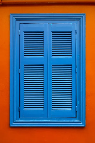 Blå fönsterluckor på en orange vägg — Stockfoto