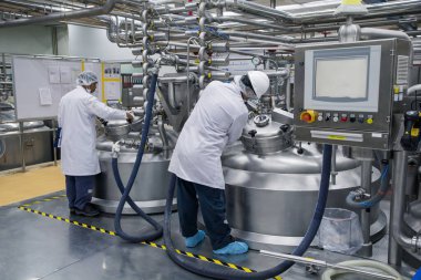 İkinci erkek, arka planda paslanmaz tankla birlikte üretimde krem kozmetik fermantasyonu üzerinde çalışıyor.