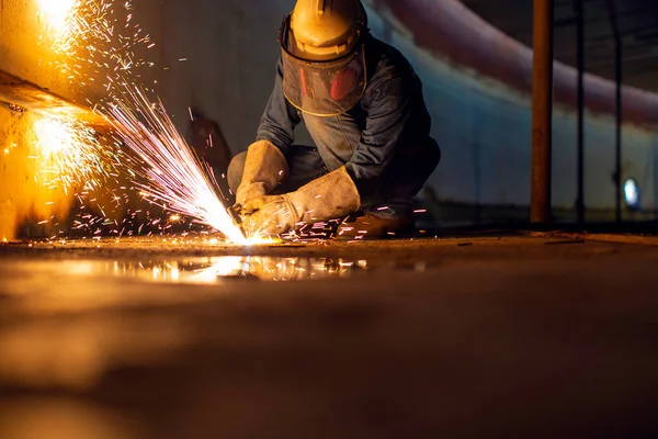 Male worker metal cutting spark on tank bottom steel plate with flash of cutting light close up wear protective gloves and mask in side confined space.
