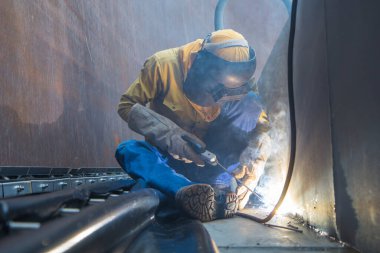 Koruyucu giysi giyen ve kaynak levhası tamir eden erkek işçi. Endüstriyel inşaat yağı ve gaz veya kapalı alanlarda depolama deposu..