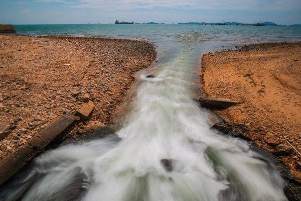 Culvert flowing industrial water slow motion out in release into the sea.