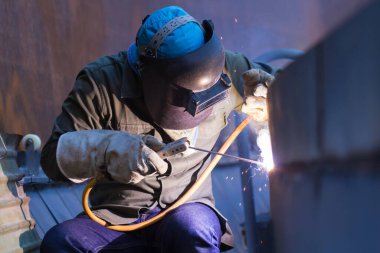 Koruyucu giysiler giyen erkek işçi ve kapalı alanlarda endüstriyel kaynakçılık yapan tank yağı tamiri.