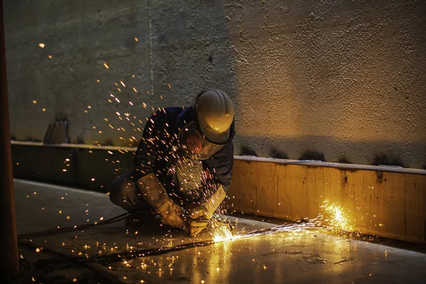 Male worker metal cutting spark on tank bottom steel plate with flash of cutting light close up wear protective gloves and mask in side confined space.