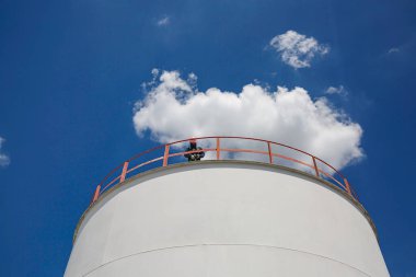 Erkek işçi endüstrisi görsel denetim çatı depolama tankı yağ bulutlu mavi gökyüzü.