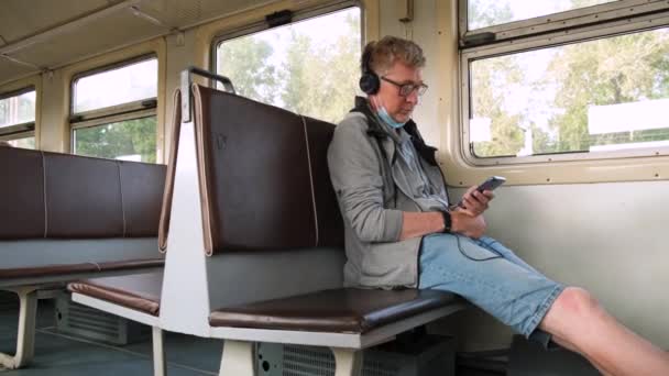 Mężczyzna Średnim Wieku Siedzi Pustym Transporcie Publicznym Słuchawkach Maską Ochronną — Wideo stockowe
