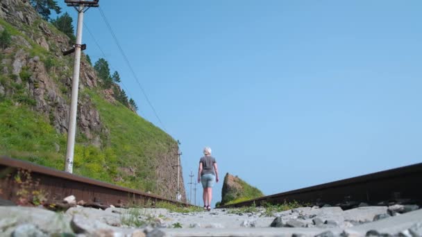孤独な女性旅行者は夏の晴れた暑い日に岩の間の鉄道線路に光を歩く 地元のハイキング 持続可能な環境 エコツーリズム — ストック動画