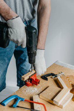 Ellerinde elektrikli ekipman tutan ve tahta bir tahtada delik açan profesyonel bir işçinin yakın çekimi. Ev yenileme ve iyileştirme konsepti. Kendin yap..