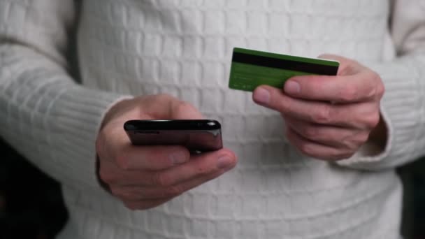 4Kクレジットカードやスマートフォンを持ち 自宅でインターネットを利用して購入する白いセーターの男の手のクローズアップ オンラインショッピングやライフスタイルの概念 近代技術 — ストック動画