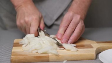 4K yakın plan erkek eli ahşap bir tahtanın üzerinde soğan doğruyor. Sebzeleri hızlıca dilimleyin. Sebzelerle sağlıklı yemekler pişirmek..