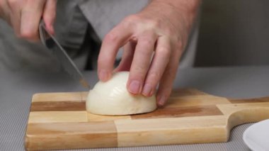 4K yakın plan erkek eli ahşap bir tahtanın üzerinde soğanları dilimliyor. Sebzeleri hızlıca dilimleyin. Sebzelerle sağlıklı yemekler pişirmek..