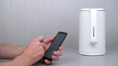 Adam akıllı telefonundaki uygulamayı kullanarak su ısıtıcısını açıyor. Nesnelerin İnterneti - Ev Wi-Fi yönetimi, aygıtlar ve akıllı telefonlu cihazlar. Akıllı ev. 4K.