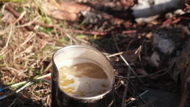 Cooking in a camping pot on a campfire in the forest outdoors. The soup is boiling and steam is coming over it. The concept of survival, hiking, traveling and cooking in nature. Slow motion.