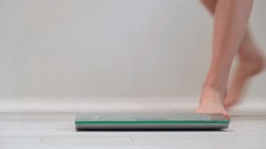 4 bin. Genç bir kız yaklaşıyor ve tartıya çıkıp ağırlığı ölçüyor. Çıplak kadın ayakları, yakın plan. Günlük ağırlık kontrolü ve sağlıklı yaşam tarzı konsepti. Günlük kullanım için modern dijital ölçekler.