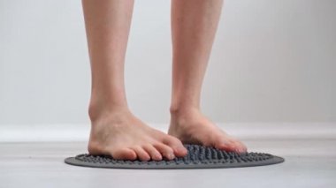4 bin. Genç kız ayaklarını ayaklarının akupunktur için tasarlanmış ortopedik masaj paspasına basar. Yakın plan. Refleksojenik bölgeler üzerindeki etkileri. Hastalıkların önlenmesi. Alternatif tıp kavramı