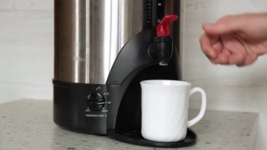 4 bin. Bir adamın eli, kahve ya da çay demlemek için modern elektrikli termopottan kaynamış bir bardağa kaynar su döküyor. Ofiste kahve molası. Bir kafede self servis. Yakın plan..