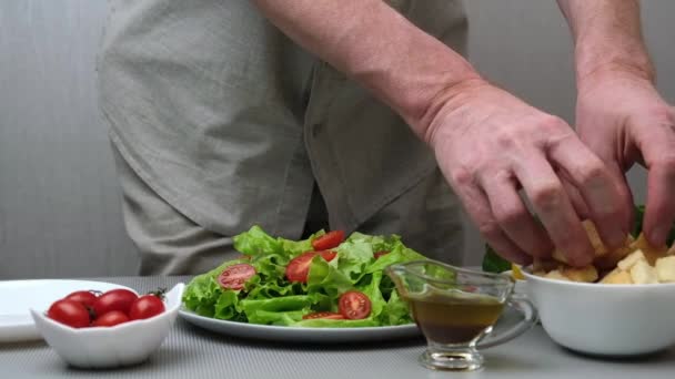 Egy férfi séf egészséges és finom vegetáriánus Caesar salátát készít. A szakács krutont tesz egy tányérba salátával. Közelkép. Lassú mozgás. Főzési folyamat. Lépésről lépésre. Recept. 3. lépés.