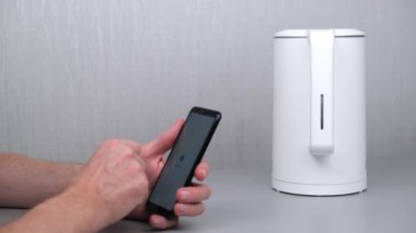 Adam akıllı telefonundaki uygulamayı kullanarak su ısıtıcısını açıyor. Nesnelerin interneti - ev kablosuz ağ yönetimi, cihazlar ve cep telefonlu cihazlar. Akıllı ev. 4K.