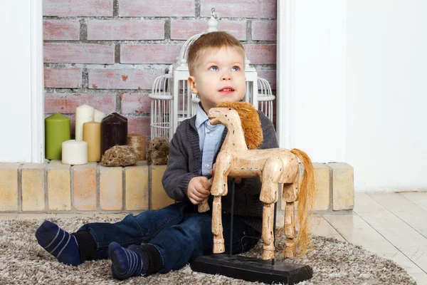 Petit garçon assis sur un plancher avec un cheval jouet — Photo