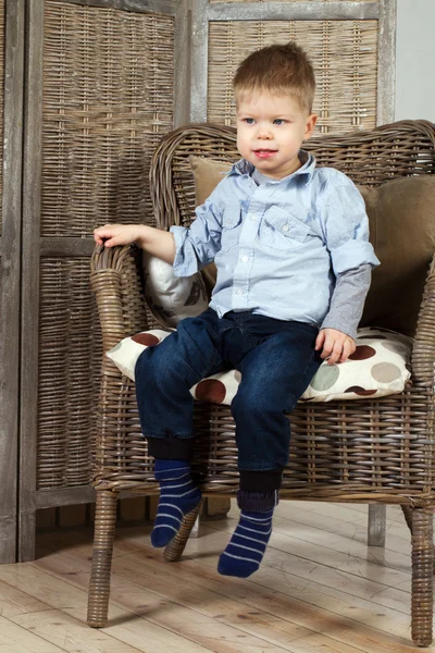 Kleine jongen zit in een leunstoel — Stockfoto