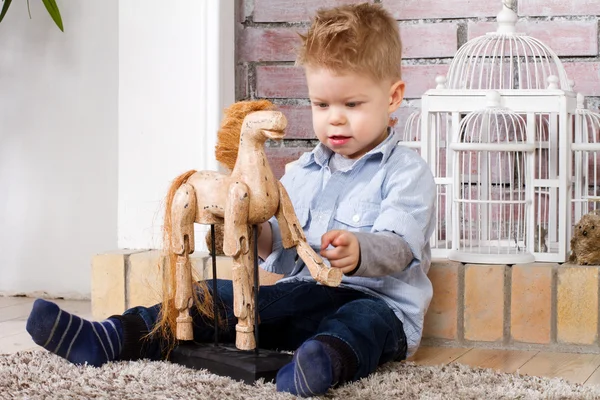 Menino senta-se em um chão com cavalo de brinquedo — Fotografia de Stock