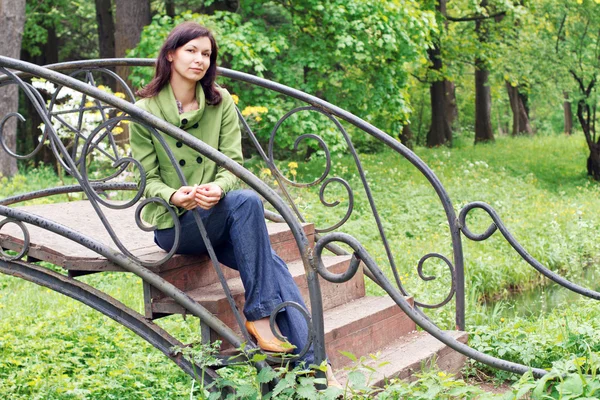 Giovane donna siede sul ponte in un giardino — Foto Stock