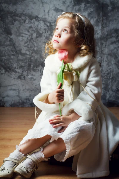 Schattig klein meisje in een witte vacht zittend op een oude koffer — Stockfoto