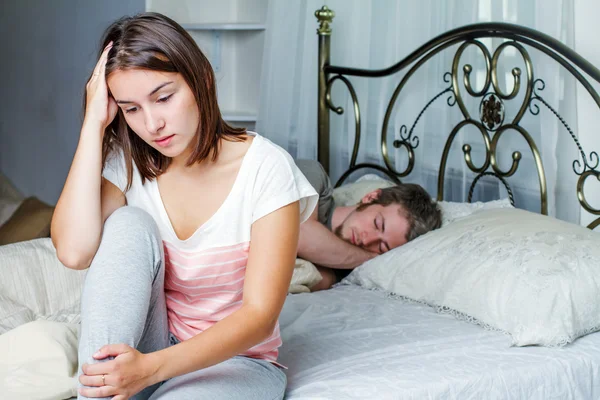 Woman sitting on a bed while her husband is sleeping — Stock Photo, Image