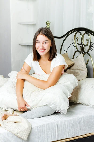 Feliz joven sentada en la cama — Foto de Stock