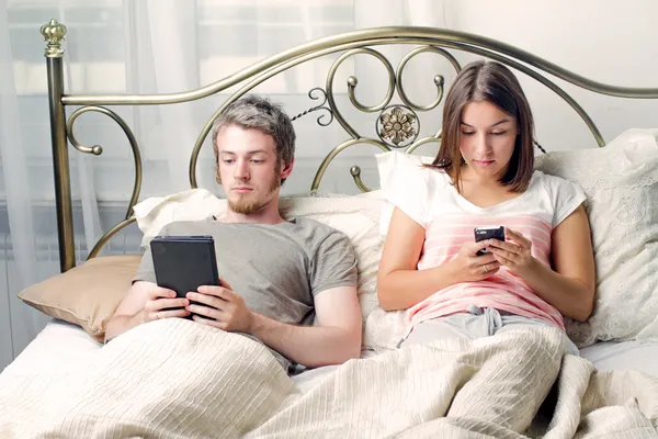 Un hombre y una mujer se acuestan en la cama y leen libros electrónicos —  Fotos de Stock