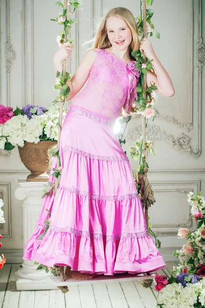 Meisje in een lang roze jurk staande op een schommel — Stockfoto