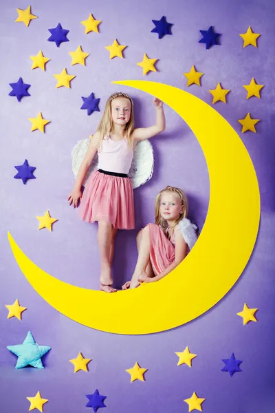 Two cute girls sitting on a big moon — Stock Photo, Image