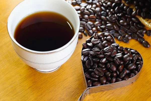 Tazza di caffè e chicchi di caffè a forma di cuore sul tavolo di legno — Foto Stock