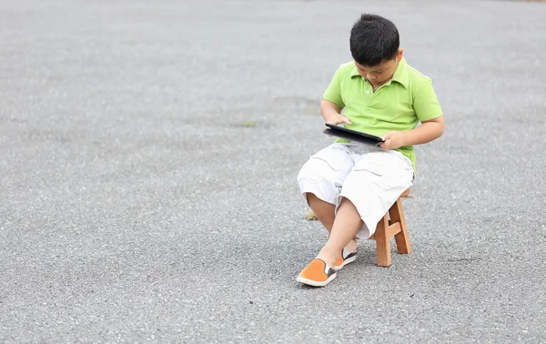 Boy sitting play a tablet on the road — Stock Photo, Image